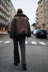 Anorak corto acolchado color marrón chocolate, con cuello subido, manga larga con puños elásticos y cierre frontal con botones ocultos y lazada lateral.