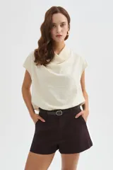 Blusa de poliéster color marfil, de corte holgado, sin mangas y con cuello buche drapeado.