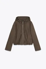 Chaqueta bomber de efecto ante en color marrón, con capucha ajustable mediante cordones, cierre frontal con cremallera, bolsillos laterales y bajo con elástico interior.