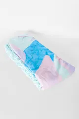 Pareo de playa con estampado abstracto en tonos celeste, azul, lila y rosa, con flecos de hilo en color celeste.