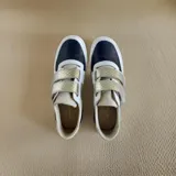 Championes de cuero con cierre de velcro, en combinación de colores blanco, negro y dorado texturizado, con detalles de arte pintado a mano en tonos turquesa y tostado en los laterales.