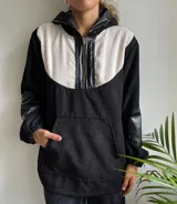 Canguro de pana negro y blanco con capucha, cierre frontal parcial con cremallera y mangas largas con puños elásticos. Presenta un bolsillo tipo canguro en la parte delantera y detalles en cuero sintético negro en la cremallera, la capucha y los codos.