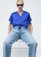 Camisa azul eléctrico de tejido satinado, manga corta, cuello camisero y cierre frontal con botones. Corte regular.