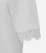 Remera de algodón blanca de corte recto y holgado, con cuello redondo y mangas cortas amplias que presentan una delicada aplicación de encaje en los dobladillos.