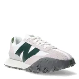 Championes urbanos New Balance modelo XC-72, con diseño combinado en blanco, gris y verde. Presentan una silueta retro-futurista con superposiciones de gamuza, paneles de cuero y una suela de goma dentada distintiva que se extiende hacia la puntera.