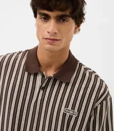 Remera de algodón con diseño rayado en tonos marrones, cuello polo en color sólido y cierre frontal con botones. Presenta un pequeño parche bordado con la palabra 'wave' en el pecho.