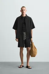 Bermuda negra de corte regular, confeccionada en tejido jacquard con efecto arrugado. Presenta cintura elástica ajustable con cordón blanco, bolsillos laterales y bolsillos traseros de vivo.