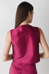 Top sin mangas de estilo cruzado, confeccionado en tela satinada color cobre. Presenta un diseño corto con cierre frontal mediante tiras finas para anudar y cuello redondo.