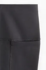 Leggins deportivos negros de tiro alto con cintura ancha y costuras frontales verticales.