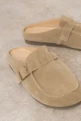 Zueco de cuero gamuzado color marrón, con diseño minimalista y elegante. Cuenta con una tira lateral con hebilla metálica regulable y plantilla acolchada. Su base es liviana y flexible.