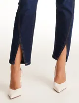 Jean skinny de tiro alto, color azul oscuro, con cierre frontal y botón. Presenta un diseño ajustado con tajos frontales en el ruedo y bolsillos funcionales.