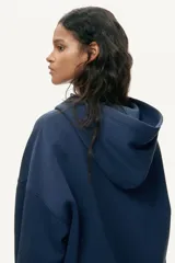 Campera canguro de felpa color azul marino con cierre frontal, capucha forrada y bolsillos delanteros tipo parche. Presenta hombros caídos, corte holgado y puños y bajo de punto acanalado.