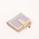 Billetera compacta de mujer, color beige con detalles en lila y azul claro. Presenta una textura de tejido en la parte frontal y un cierre de cremallera con un dije en forma de imperdible dorado.