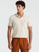 Chomba color crema de manga corta con cuello clásico y logo bordado en el pecho. Detalles de rayas en cuello y mangas.