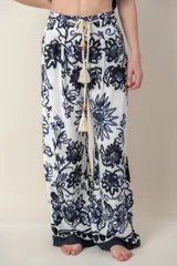 Pantalón ancho de tela blanca con estampado de flores azules, cintura alta con cordón ajustable y bolsillos laterales.