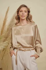Blusa de satén color champagne con cuello a la base, mangas anchas y puños elásticos con detalle bordado.