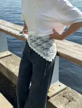 Pañuelo de encaje blanco con diseño floral, de forma triangular, ideal para usar como accesorio sobre la cintura o como detalle decorativo en la vestimenta.