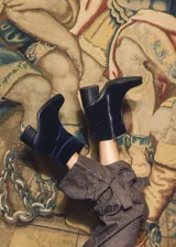 Bota corta de velvet azul marino con efecto abullonado en el tobillo y cierre lateral con cremallera. Tiene un tacón cuadrado y una cadena desmontable con el logo de la marca.