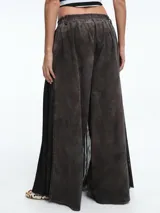 Pantalón de corte amplio y tiro medio, confeccionado en una base de algodón con una capa de tul negro superpuesta que aporta volumen y movimiento, simulando una falda larga.