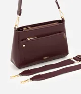 Cartera bandolera de poliuretano color marrón oscuro, con estructura firme y tamaño mediano. Cuenta con un bolsillo frontal con cierre, herrajes metálicos dorados, cierre principal y correa ajustable y desmontable.
