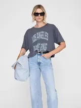 Remera gris oscura de algodón con calce amplio, cuello redondo y estampa tipográfica frontal estilo universitario en tonos claros.