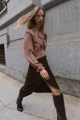 Blusa de manga larga con estampado de cuadros vichy en tonos burdeos y beige. Presenta cuello mao y grandes volantes fruncidos que cruzan el pecho y los hombros. Los puños son elásticos y fruncidos.