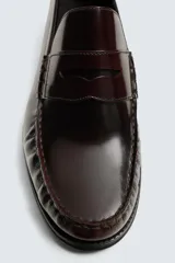 Mocasín de vestir fabricado en piel color bordó, con detalle de antifaz en el empeine y suela a tono con ligero tacón.