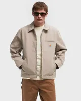 Campera Carhartt modelo Detroit color beige, con cuello camisero, cierre frontal con cremallera, bolsillos laterales y bolsillo en el pecho con logo de la marca.