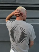 Remera gris de manga corta con corte regular, de la marca Kaboa Industries, con estampa en la espalda que presenta un esqueleto dentro de un ataúd rodeado por alas oscuras y las leyendas WAKE UP y Kaboa Industries.