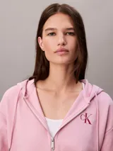 Buzo con capucha de Calvin Klein, de corte cropped y color rosado, confeccionado en mezcla de algodón y poliéster. Cuenta con cierre frontal de cremallera, cordones ajustables en la capucha y bolsillos tipo canguro. Presenta el logo de la marca bordado discretamente en el pecho.