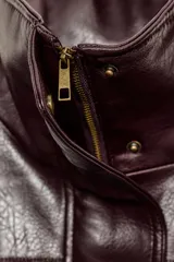 Chaqueta de efecto piel en color bordó, con cuello subido, manga larga con puños y bajo elástico. Presenta cierre frontal con cremallera y botones a presión ocultos, además de bolsillos laterales.