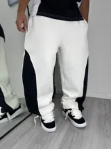 Pantalón tipo jogger de corte baggy, con diseño bicolor en blanco y negro. Presenta paneles laterales en contraste y una silueta holgada.
