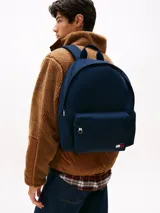 Mochila de diseño redondeado color azul marino, con asa superior, correas ajustables y acolchadas. Presenta un compartimento principal con cierre, bolsillo exterior con cremallera y parche con el logo de Tommy Jeans en la parte delantera.