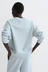 Buzo de corte oversized con cuello redondo, hombros caídos y puños y bajo acanalados. Presenta un diseño liso con interior cepillado suave.