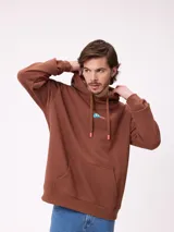 Canguro marrón con capucha y bolsillo frontal, con un diseño gráfico colorido en la espalda que representa una casa surrealista con el texto 'Supreal State of Mind'.