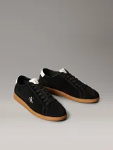 Zapatillas Calvin Klein de perfil bajo elaboradas en ante negro, con suela cupsole de goma marrón. Presentan detalles en contraste de color blanco en el talón y la lengüeta, además del monograma 'ck' bordado en el lateral.