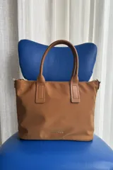 Cartera tipo shopper color negro, de diseño estructurado con doble asa de mano y cierre superior. Presenta sutil grabado de la marca en la parte inferior frontal.