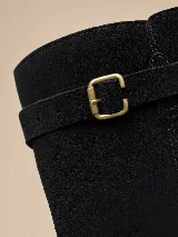 Bota alta de gamuza color marrón, con caña ancha, taco bajo cuadrado y punta fina. Cuenta con tres tiras con hebillas metálicas doradas ajustables: una en la parte superior, otra a la altura del tobillo y otra sobre el empeine.