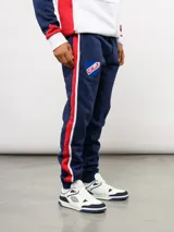 Pantalon de jogging azul de felpa, con franjas laterales en blanco y azul marino. Presenta el escudo del Club Nacional de Football en el muslo derecho y el logo de Umbro en el izquierdo.
