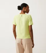 Blusa blanca de poliéster con cuello redondo, mangas cortas, cierre trasero en forma de gota, pequeñas aberturas laterales y acabados en pespuntes en las mangas y el cuello.