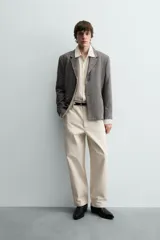 Pantalón chino de corte relajado, confeccionado en tejido estructurado de color beige. Presenta bolsillos frontales, bolsillos traseros de vivo y cierre frontal con cremallera y botón.