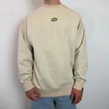 Buzo de corte oversize color beige, con estampa gráfica en la espalda que incluye botellas de vino y texto descriptivo.