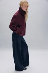 Abrigo corto de paño con mezcla de lana, color bordó. Presenta cuello subido, cierre frontal cruzado con botones, mangas largas con trabillas decorativas y bolsillos laterales de vivo.