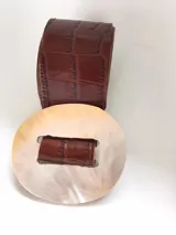 Cinturón marrón con textura de cocodrilo y hebilla redonda de nácar.
