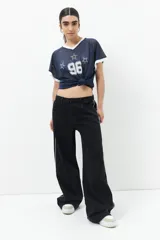 Pantalón de jean negro de tiro bajo y corte ancho, con línea bordada blanca en ambas piernas y cinco bolsillos.