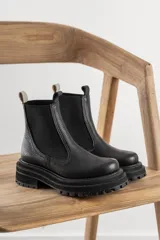 Botas tipo Chelsea de cuero negro con textura granulada, paneles laterales elásticos y suela track de goma gruesa con plataforma.