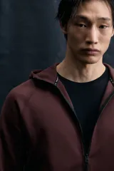 Campera deportiva de tejido funcional con efecto neopreno, con capucha, cierre frontal y bolsillos laterales con cierre. Presenta mangas raglán y terminaciones elásticas en puños y bajo.