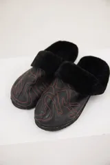 Pantuflas de cuero negro con interior de piel sintética, diseño con bordados decorativos en color naranja y suela plana.