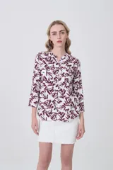 Camisa de viscosa con estampado botánico en tonos bordó sobre fondo blanco, cuello mao y cierre frontal con botones. Presenta bolsillos frontales y mangas tres cuartos.