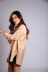 Camisa beige de corte amplio, con cuello clásico, cierre frontal con botones, mangas largas con puños abotonados y bordado floral en las mangas.